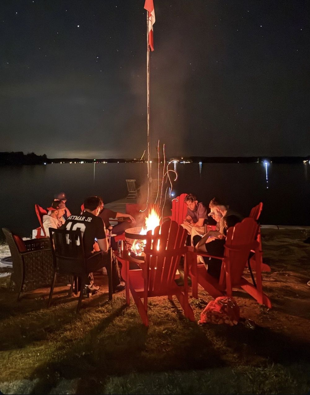 Campfire with friends by a lake at night, Canadian flag in the background